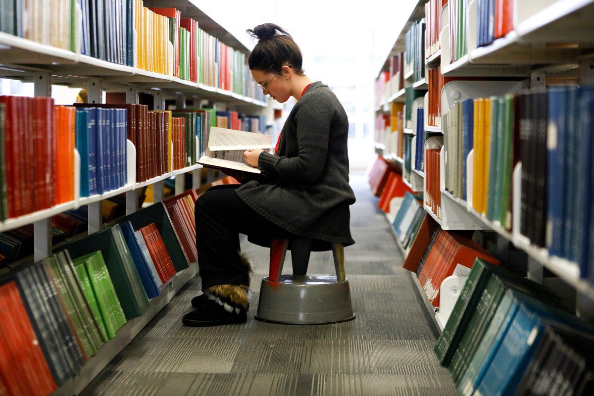 student reading a book in the library between two bookshelves