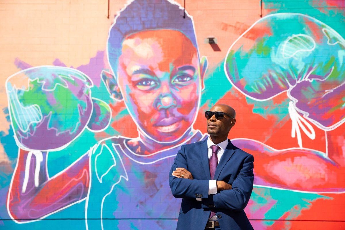 MSU Denver alumnus Eric Williams standing in front of street art of a boy with boxing gloves on his hands.