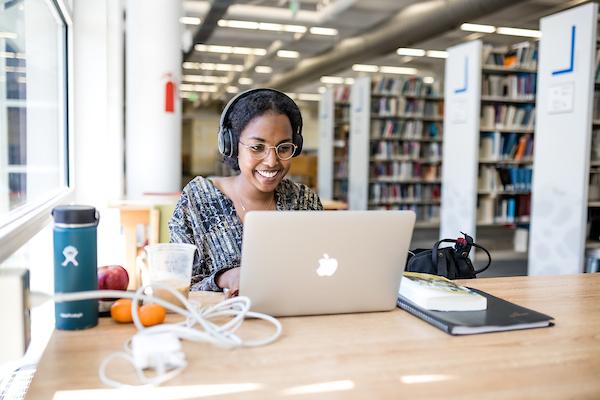 微笑的学生在图书馆用笔记本电脑工作