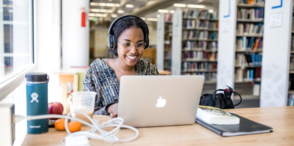 Smiling female student on a MacBook in a library