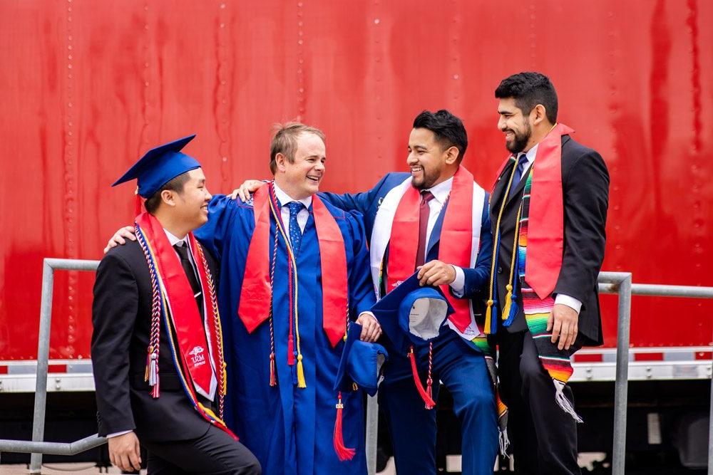A group of four male graduates smiling and laughing at commencement in May 2023