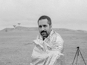 Professor Nima Bahrehmand outside in a desert setting wrapped in a reflective blanket next to a tripod.